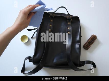 Zaino da donna in pelle di cavallo pazzo. Sta tenendo la spugna. Lo zaino è nero, sul retro. Hardware dorato. Cera e spazzolina per la pulizia nelle vicinanze. Foto Stock