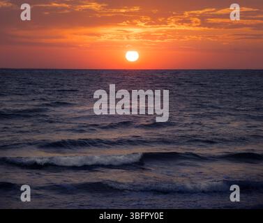 Le sfumature dorate si fondono con il mare calmo mentre il sole tramonta sulla Sicilia, gettando un magico bagliore sulle acque tranquille dell'Italia Foto Stock