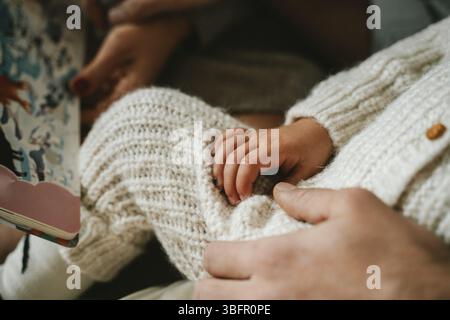 Immagine ravvicinata della mano di un bambino che poggia delicatamente su quella di un adulto, catturando un tenero momento di legame. Le morbide texture e il calore del tessuto lavorato a maglia Foto Stock