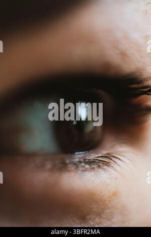 Foto dettagliata e ravvicinata dell'occhio di un bambino, che cattura i dettagli intricati dell'iride e delle ciglia. Un riflesso distinto può essere visto nell'occhio Foto Stock