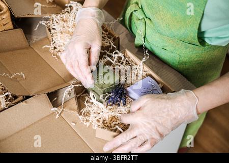 Le mani con i guanti consentono di disporre saponi verdi e lavanda con fiori secchi in confezioni kraft. Prodotti artigianali, imballaggi ecologici, prodotti per la cura della pelle naturali Foto Stock