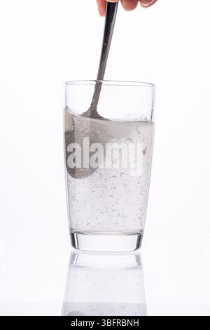 Il collagene o la polvere medicinale viene mescolato con un cucchiaio in un bicchiere d'acqua su sfondo bianco. Foto di alta qualità Foto Stock