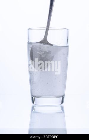 Il collagene o la polvere medicinale viene mescolato con un cucchiaio in un bicchiere d'acqua su sfondo bianco. Foto di alta qualità Foto Stock