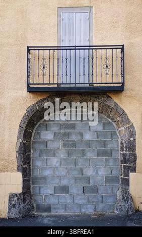 Un balcone con ringhiera in metallo si erge su un'entrata in pietra bloccata su un edificio giallo testurizzato, creando una caratteristica architettonica suggestiva in un'area urbana. Foto Stock