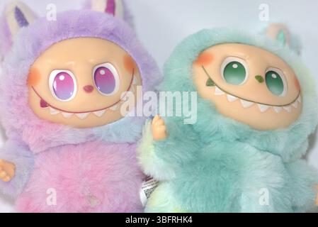 Due giocose figure di giocattoli Labubu in morbidi costumi da mostro verde e rosa e un sorriso malizioso, posate su uno sfondo bianco. Foto Stock