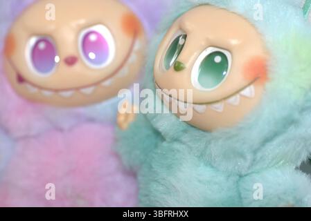 Due giocose figure di giocattoli Labubu in morbidi costumi da mostro verde e rosa e un sorriso malizioso, posate su uno sfondo bianco. Foto Stock