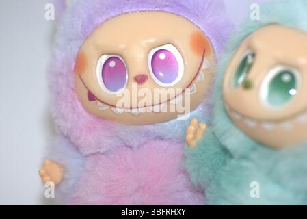 Due giocose figure di giocattoli Labubu in morbidi costumi da mostro verde e rosa e un sorriso malizioso, posate su uno sfondo bianco. Foto Stock