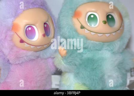 Due giocose figure di giocattoli Labubu in morbidi costumi da mostro verde e rosa e un sorriso malizioso, posate su uno sfondo bianco. Foto Stock