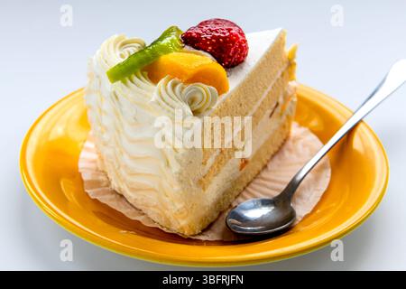 Primo piano di una fetta di torta alla frutta con fragole, pesca e kiwi isolati su bianco. Foto Stock