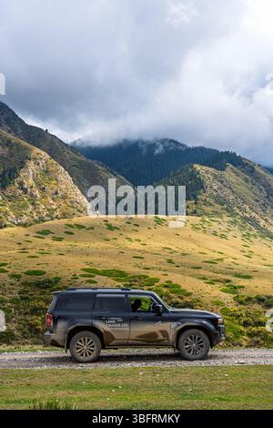 Bishkek, Kirghizistan - 12 ottobre 2024: Una Toyota Land Cruiser 250 nera che guida su una strada sterrata, con vaste, verdi e gialle pendici di montagna sotto un c Foto Stock