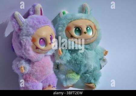 Due giocose figure di giocattoli Labubu in morbidi costumi da mostro blu e rosa e un sorriso malizioso, posate su uno sfondo bianco. Foto Stock