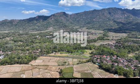 Maestoso panorama aereo che cattura la distesa di campi terrazzati, un tranquillo villaggio, e lo sfondo spettacolare delle montagne vulcaniche sotto una chiara b Foto Stock