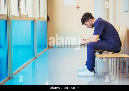 Medico stanco seduto nel corridoio dell'ospedale riflettendo su casi difficili Foto Stock