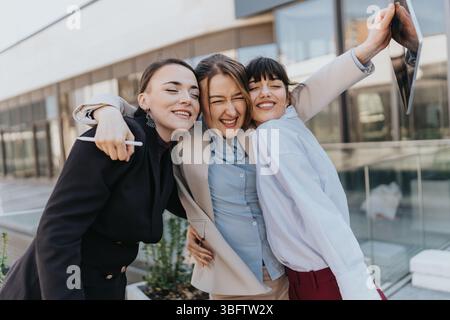Tre freelance che condividono un momento di gioia all'aperto, abbracciando e sorridendo, rappresentando amicizia, successo ed energia positiva. Foto Stock