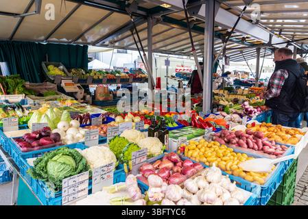 Salisburgo, Austria - 2 aprile 2025: Negozio di frutta e verdura con cavolfiore a Grunmarkt, mercato di Street food con gente intorno a Universitatsplatz Foto Stock