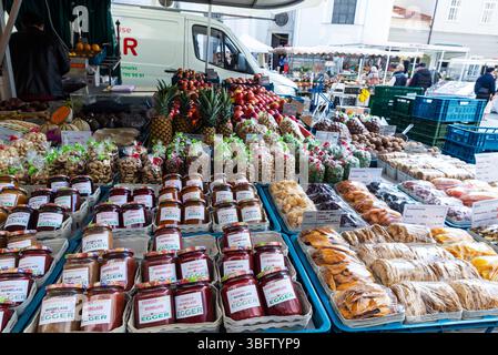 Salisburgo, Austria - 2 aprile 2025: Negozio di frutta e verdura con marmellate e noci a Grunmarkt, mercato di Street food con gente intorno a Universitatsplatz Foto Stock