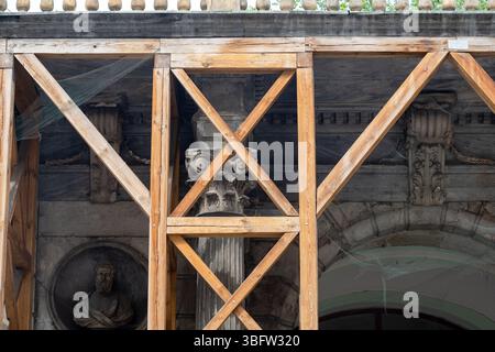 Impalcature in legno che sostengono una facciata di un vecchio edificio storico con colonne antiche, dettagli architettonici classici, decorazioni in pietra, rete durante Foto Stock