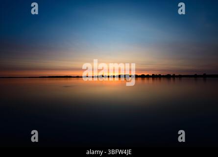 Lunga esposizione al tramonto sul lungomare con riflessi di sole e cielo sul fiume Ottawa a Petrie Island, Ottawa (Orleans), Ontario, Canada Foto Stock