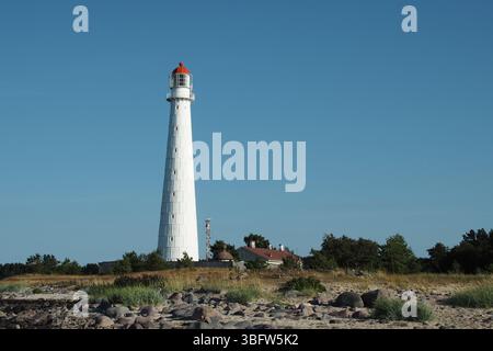 Faro bianco con cima rossa sulla costa rocciosa sotto il cielo azzurro Foto Stock