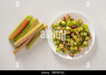 Rabarbaro appena tritato in piatto bianco su sfondo bianco. Cibo biologico alla moda. Pronti per cucinare. Concetto vegano. Vista dall'alto. Foto Stock