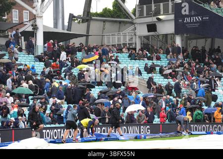 Gli spettatori si coprono sotto gli ombrelli mentre la pioggia si ferma durante la partita internazionale del terzo giorno maschile al Kia Oval di Londra. Data foto: Martedì 3 giugno 2025. Foto Stock