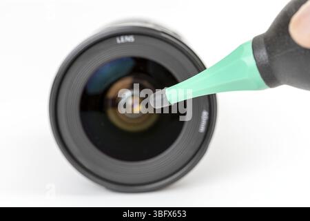 L'obiettivo di una fotocamera viene pulito con un aspirapolvere, concentrandosi sulla superficie dell'obiettivo. la soffiante è dotata di ugello verde e lo sfondo è bianco, sottolineando il processo di pulizia Foto Stock