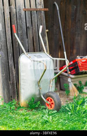Vari attrezzi da giardinaggio in piedi vicino alla parete di legno di un fienile presso il cottage Foto Stock