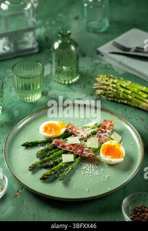 Insalata di asparagi verdi deliziosa e sana con pancetta, parmigiano e uova sode soffici servite su un piatto verde Foto Stock