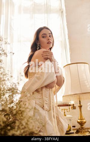 Una giovane donna pronta in un elegante abito vintage si erge delicatamente illuminata. Foto Stock