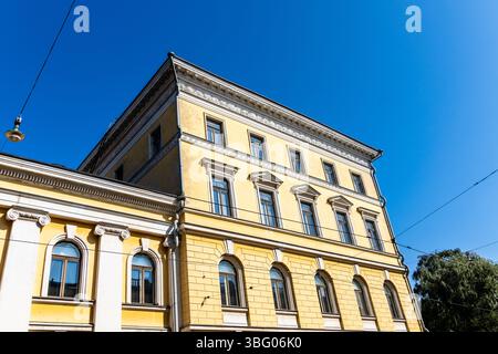 Una veduta verso l'alto di una classica facciata gialla dell'edificio con finiture dettagliate, adagiata su un cielo blu limpido a Helsinki, Finlandia. Foto Stock
