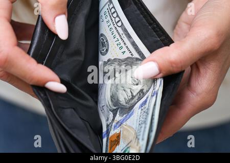Donna che tiene il portafoglio con i dollari. Borsa nera in pelle piena di contanti. Finanza personale e denaro. Primo piano di mani e bollette. Valuta americana. Foto Stock