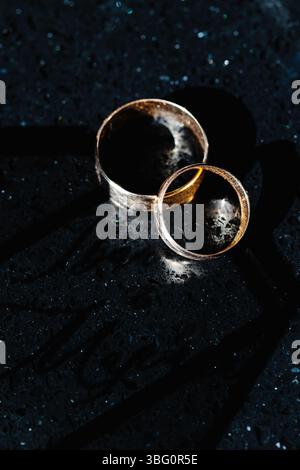 Due fedi nuziali che riflettono la luce sulla superficie di marmo scuro, che rappresentano impegno, amore e matrimonio Foto Stock