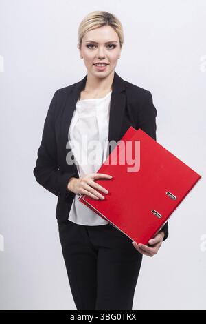 Giovane donna d'affari bionda carina caucasica con stativo in tuta nera con piegatrice isolata su un'immagine verticale nera Foto Stock