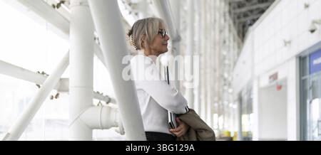 Una donna d'affari di mezza età si trova in un ufficio elegante e sta esaminando documenti importanti. Sembra concentrata e impegnata in un set professionale Foto Stock