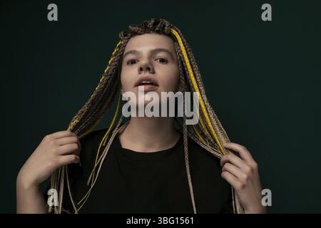 Una donna con i dreadlock è in piedi in posizione verticale davanti a uno sfondo verde brillante. I suoi capelli sono modellati in lunghi e spessi dreadlock che le cadono a cascata Foto Stock