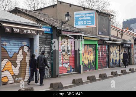 La coppia passeggia davanti alle porte arrotolate di antiquariato chiuso e ai negozi di seconda mano del Marché aux puces a Saint-Ouen-sur-Seine, Francia Foto Stock
