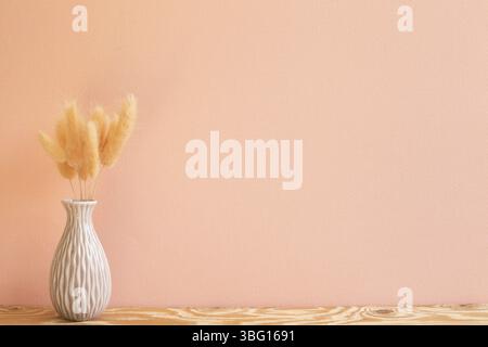 Vaso di prugnole rosa (Lagurus ovatus) fiori secchi su tavola di legno. Sfondo rosa Foto Stock