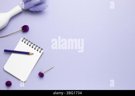 Taccuino, matita colorata, fiori secchi su sfondo viola. Posa piatta, vista dall'alto, spazio per la copia Foto Stock
