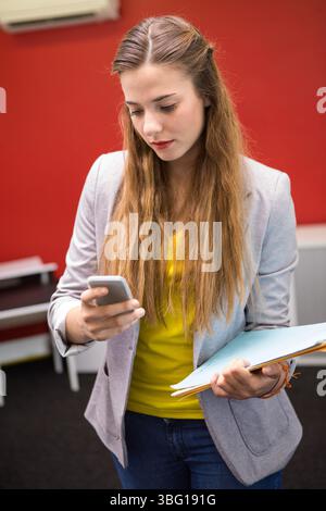 Donna che indossa blazer e jeans con smartphone e cartella in ufficio sotto la bocchetta di ventilazione dell'aria condizionata Foto Stock