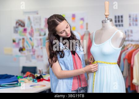 Donna che misura un abito blu pallido su manichino in uno studio di design con nastro giallo e campioni Foto Stock
