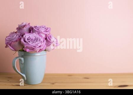 Fiori di rosa viola in tazza di ceramica su tavolo di legno con sfondo rosa. Disposizione floreale primavera, spazio copia Foto Stock