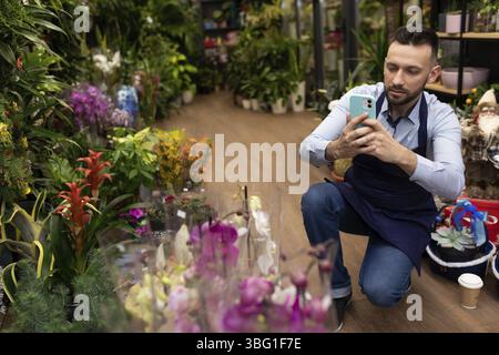 Uomo che scatta foto di piante in vaso con il telefono cellulare Foto Stock