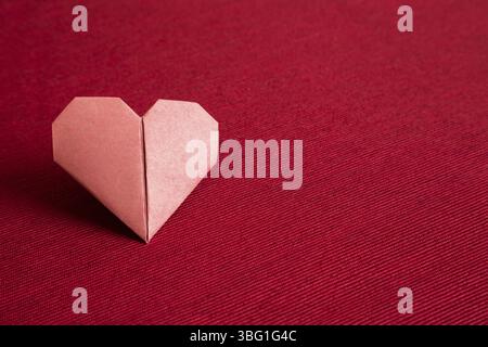 Carta rossa cuore origami su fondo tessuto rosso. Copia spazio Foto Stock