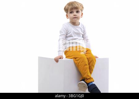 Triste ragazzo biondo annoiato seduto su sfondo bianco Foto Stock
