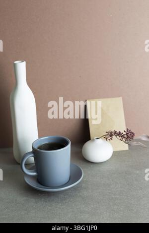 Still Life di tazza di caffè e busta e vaso in ceramica con pianta secca. Sfondo grigio Foto Stock
