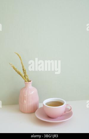 Tazza di tè rosa e vaso di fiore secco su tavola bianca. sfondo parete menta. spazio di copia Foto Stock