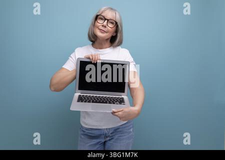 Affari di mezza età. donna di mezza età con capelli grigi che padroneggia la tecnica del laptop su sfondo studio con spazio per copie Foto Stock