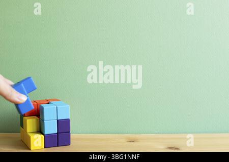 Colorati blocchi di puzzle a cubo su una scrivania di legno con sfondo verde. Risoluzione dei problemi, concetto di idea creativa Foto Stock