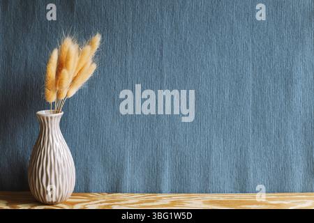 Vaso di lepri rosa (Lagurus ovatus) fiori secchi su tavolo di legno con fondo in tessuto blu navy Foto Stock