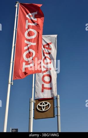 Bandiere con marchio Toyota fuori da una concessionaria ufficiale, contro il cielo azzurro, che rappresentano la presenza automobilistica dell'azienda e il marchio aziendale Foto Stock